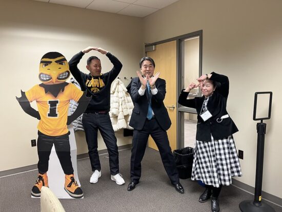 Three International Visitors from Japan pose with a cardboard cutout of University of Iowa mascot Herky the Hawk.